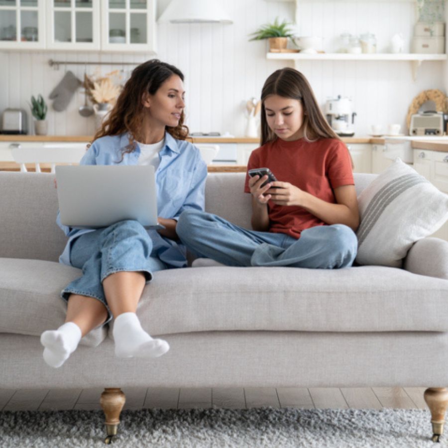 En mor og datter ser på pc og mobil i sofaen