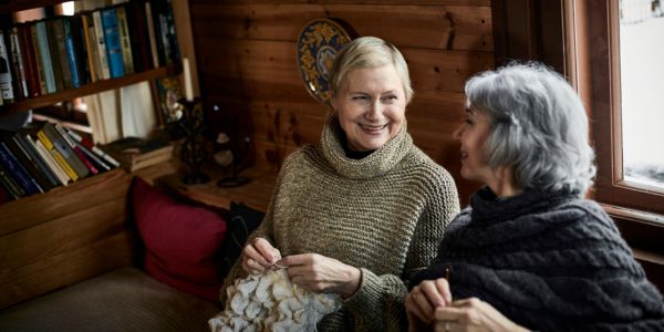 To kvinner sitter sammen og strikker i en hytte