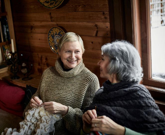 To kvinner sitter sammen og strikker i en hytte